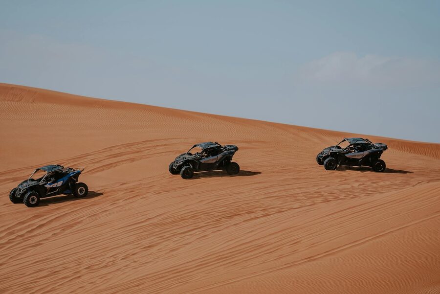 Three ATVs racing across desert dunes