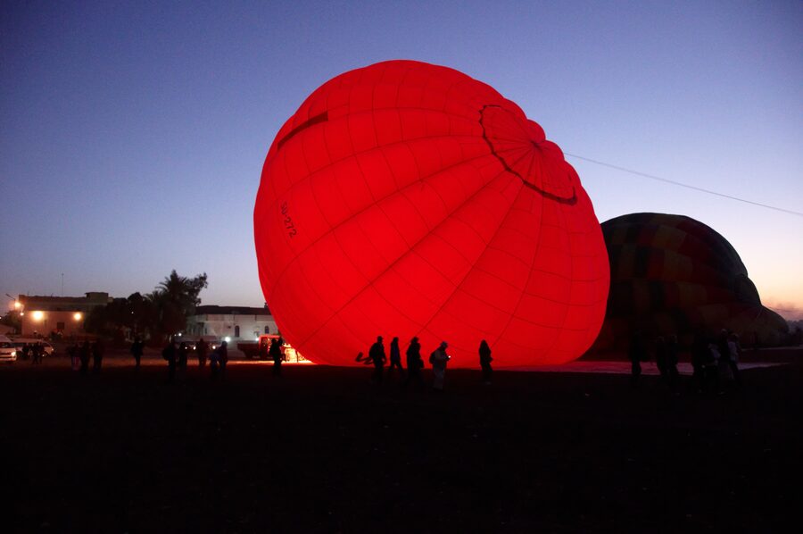 Hot air balloon being inflated by ground crew in pre-dawn light near Luxor