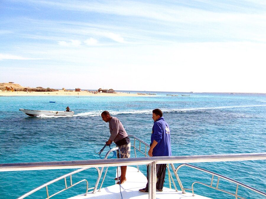 Tourists wading in shallow turquoise water near snorkel boats at Giftun