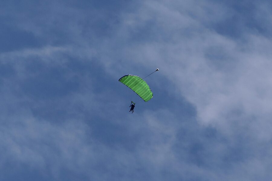 Tandem parachute descent with open canopy above scenic landscape