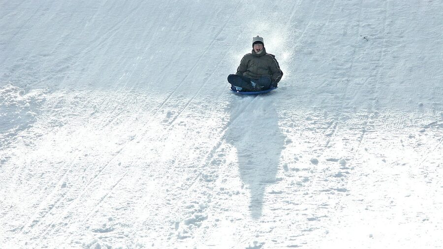 Child enjoying snow tubing toboggan ride down snowy hill