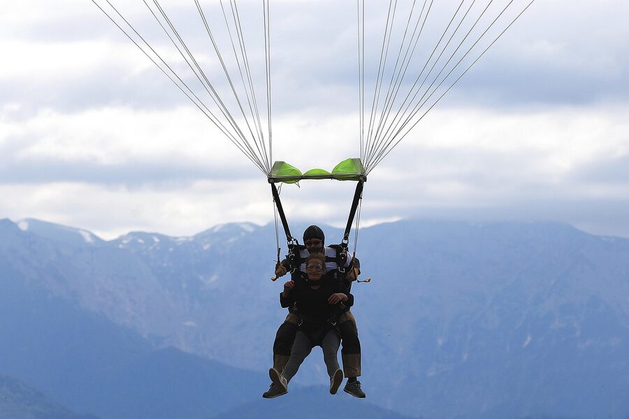 Tandem skydivers landing with parachute on green field